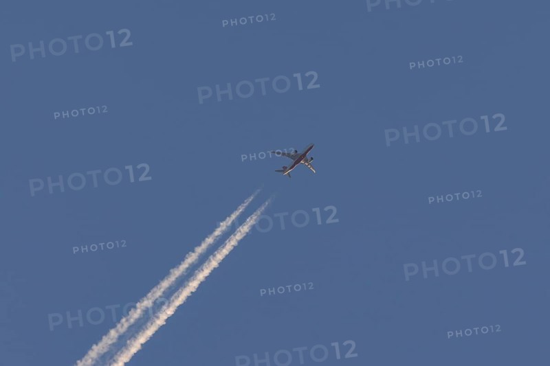 Boeing 787-8 Dreamliner aircraft flying across a blue sky with a vapour trail or contrail behind, England, United Kingdom, Europe