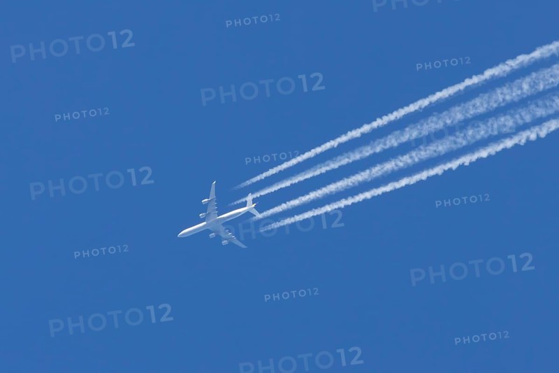 Airbus A340 aircraft flying across a blue sky leaving a contrail or vapor trail in the atmosphere behind the plane, England, United Kingdom, Europe