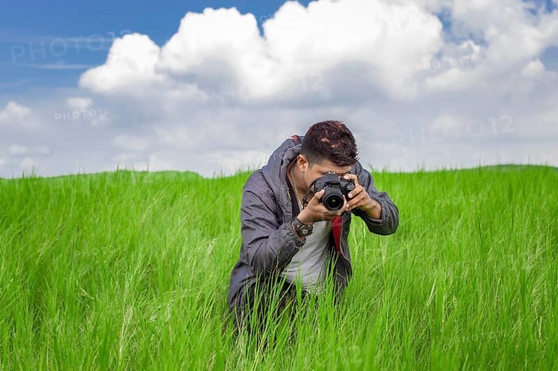 Man taking picture with camera in the field, photographer in the field taking a picture, Latino man in a green field taking a picture