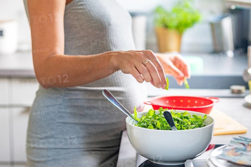A pregnant woman prepares a healthy meal with fresh ingredients in the kitchen