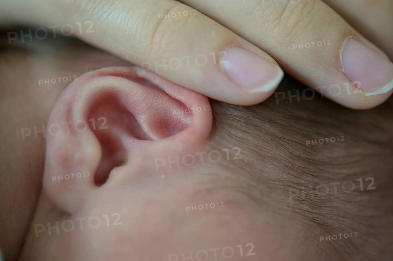 Close-up of a baby whose ear is gently touched by a hand