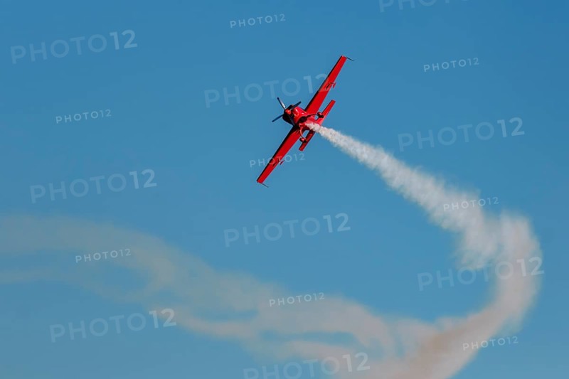 Red stunt aerobatic plane performing stunts in blue sky. Concept of speed, difficulty, precision, risk