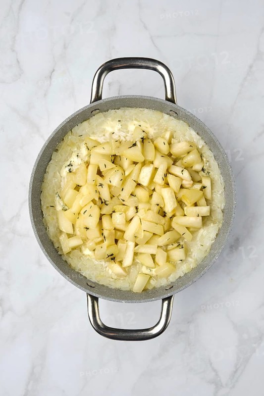 A silver pot filled with creamy rice topped with freshly diced pears and herbs on a marble countertop. The dish appears warm and inviting, showcasing a blend of textures and flavors.