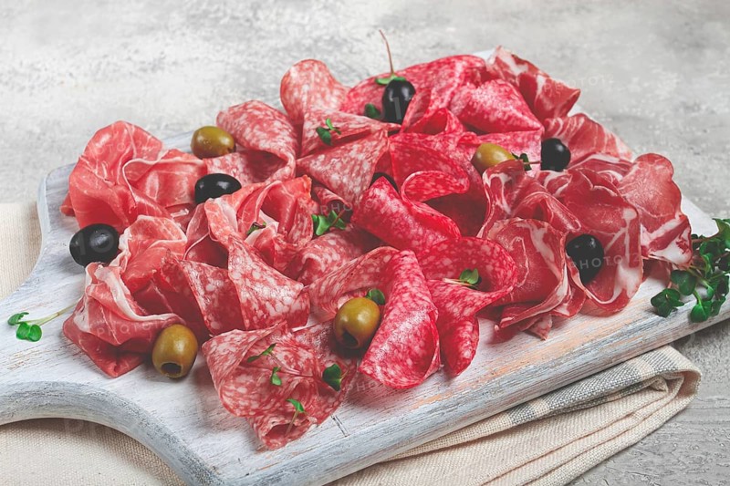 Assorted, meat appetizer, prosciutto, salami and ham, with olives, on a wooden white board, light background, breakfast, top view, close-up, no people