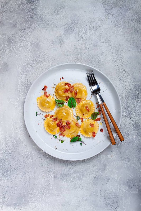 Fresh ravioli, with butter, spices and herbs, fried bacon, on the table, top view, light background, no people