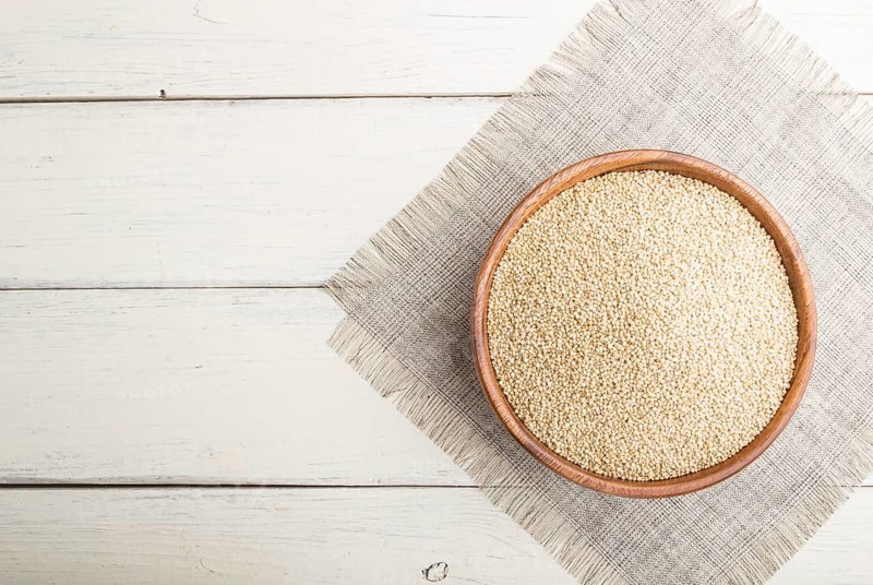 Wooden bowl with raw white quinoa seeds on a white wooden background and linen textile. Top view, flat lay, copy space