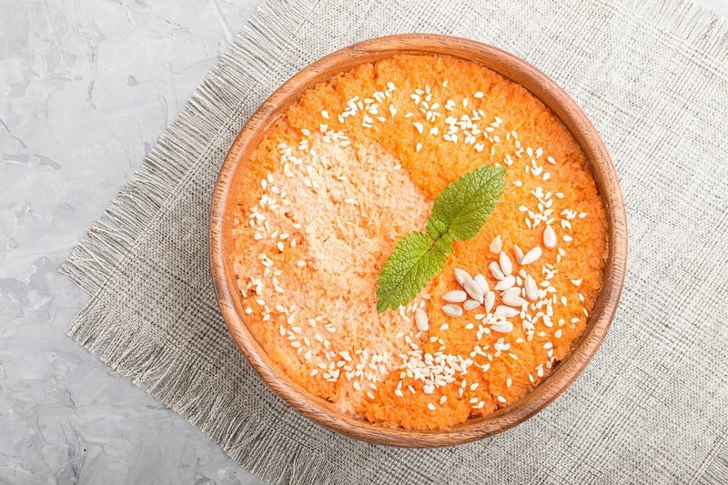 Carrot cream soup with sesame seeds in wooden bowl on a gray concrete background with linen textile. top view, flat lay, close up