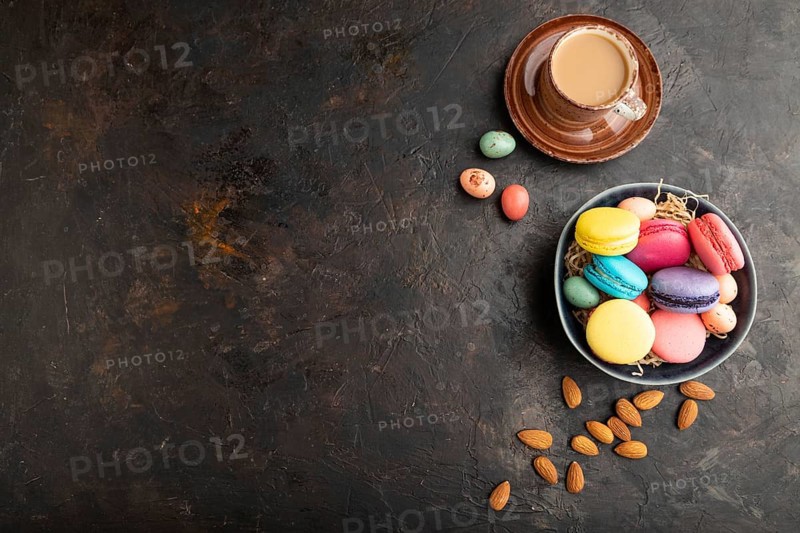 Multicolored macaroons and chocolate eggs in ceramic bowl, cup of coffee on black concrete background. top view, flat lay, copy space, still life. Breakfast, morning, concept