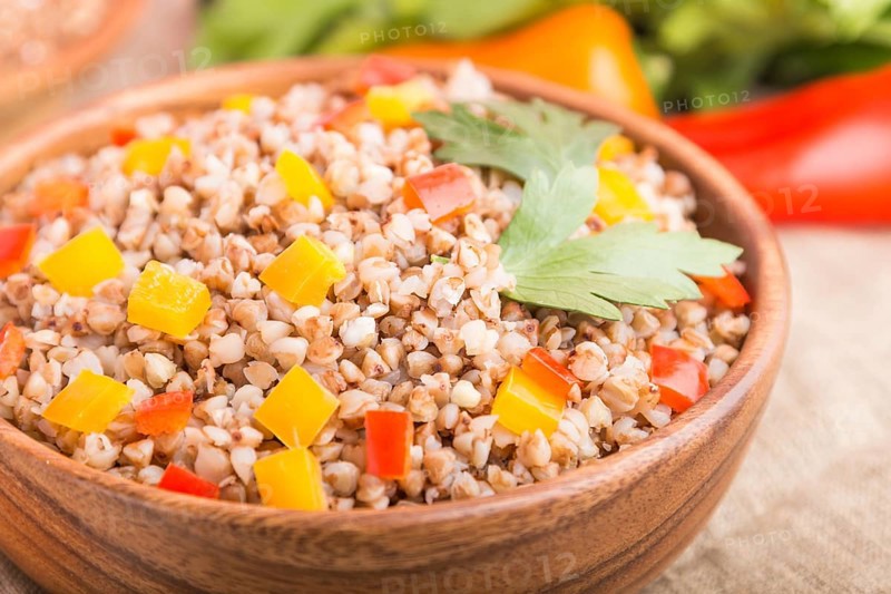 Buckwheat porridge with vegetables in wooden bowl on a white wooden background and linen textile. Side view, close up, selective focus, macro. Russian traditional cuisine