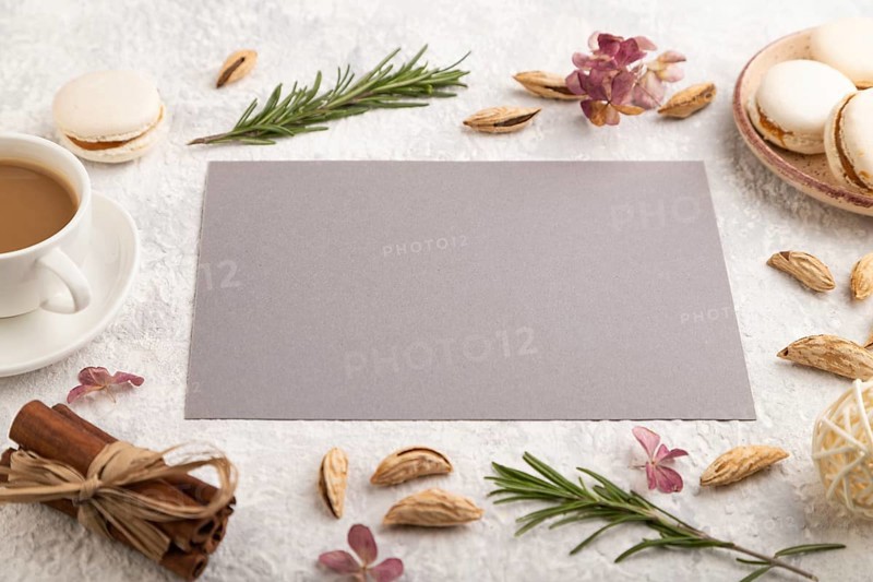 Gray paper sheet mockup with cup of coffee, almonds and macaroons on gray concrete background. Blank, business card, side view, still life