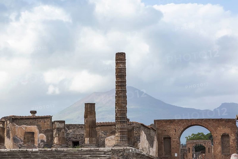 Old stone columns supported by braces and terracotta brick wall building structures plus view of Mount Vesuvius in the background at the ancient ruins of Pompeii in late summer, Campania region, Italy, Europe