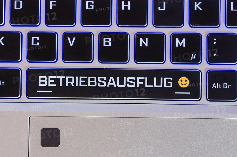 Company outing symbol image: Keyboard labelled BETRIEBSAUSFLUG, with a cheerful emoji next to it (Composing)