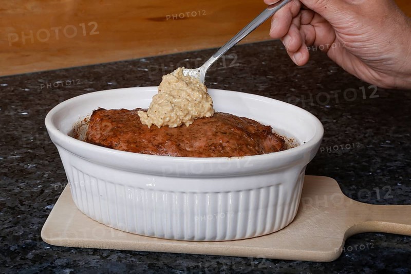Swabian cuisine, preparation of Stuttgarter Leberkäs in a horseradish-mustard coating, horseradish-mustard mixture on baked Leberkäse, Leberkäse, meatloaf, mustard crust, grandmother's kitchen, regional, home cooking, man's hand, casserole dish, spoon, typical Swabian, traditional cuisine, food photography, studio, Germany, Europe