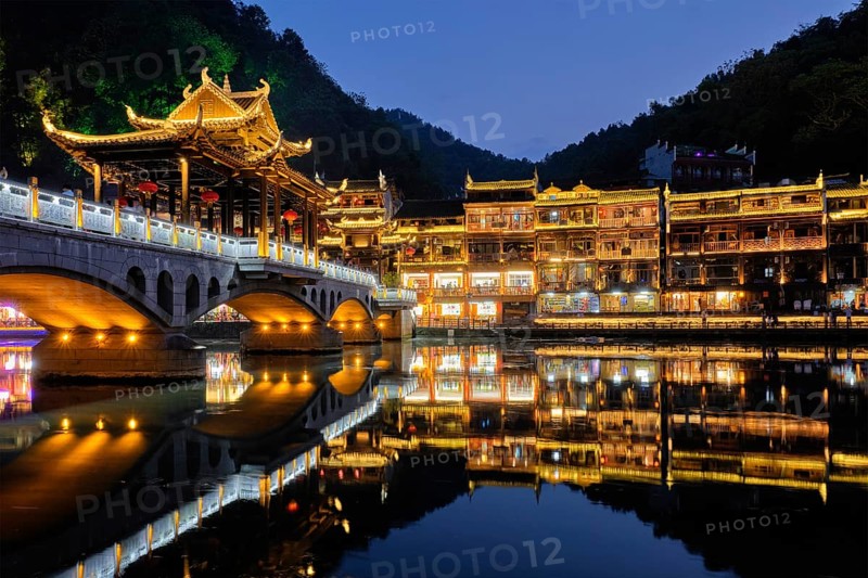 Chinese tourist attraction destination, Feng Huang Ancient Town (Phoenix Ancient Town) on Tuo Jiang River with bridge illuminated at night. Hunan Province, China, Asia