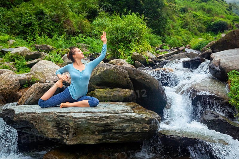 Hatha yoga outdoors, young sporty fit woman doing yoga asana Eka pada rajakapotasana, one-legged king pigeon pose at tropical waterfall. Himachal Pradesh, India, Asia
