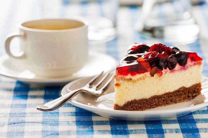 Dessert background, fruit cheese cake on plate with fork and coffee cup on blue checkered tablecloth