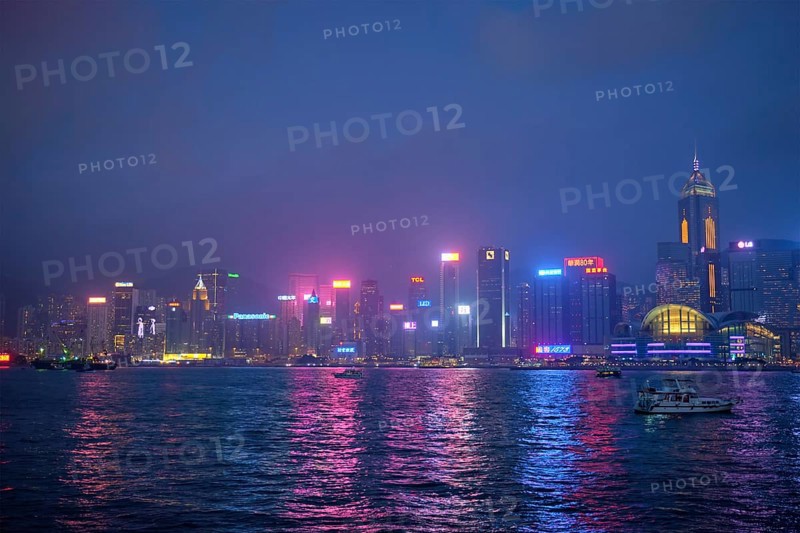 HONG KONG, CHINA, APRIL 28, 2018: Hong Kong skyline cityscape downtown skyscrapers over Victoria Harbour in the evening illuminated with tourist boat ferries, Hong Kong, China, Asia