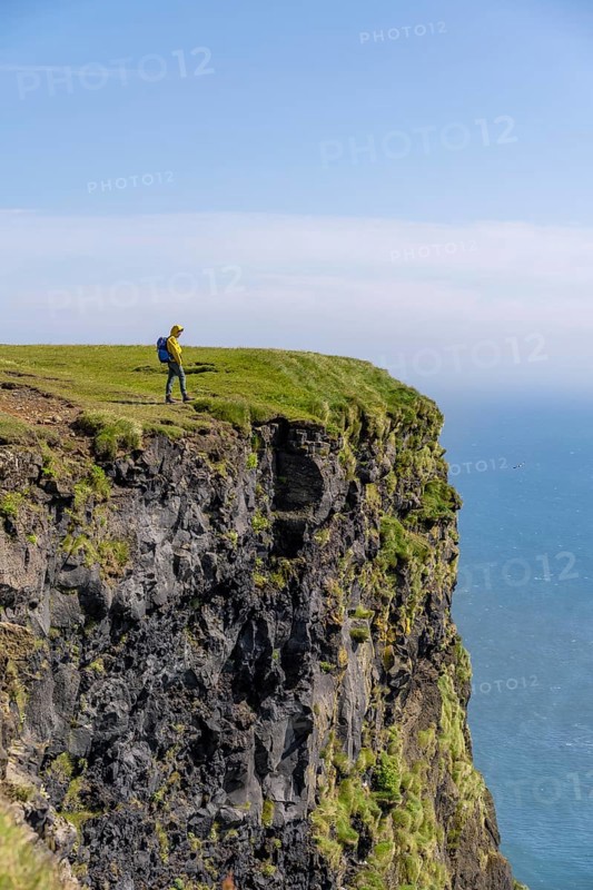 Tourist at the edge of a rock cliff, steep coast, at Reynisfjara beach, Vik, South Iceland, Iceland, Europe