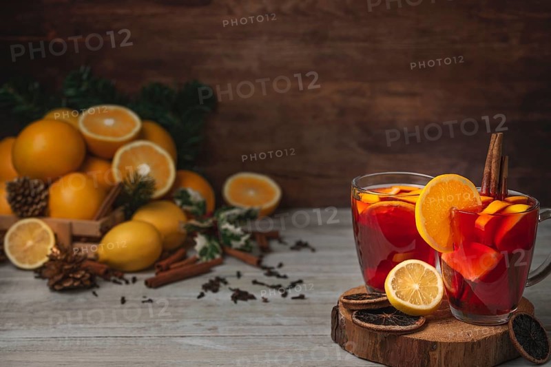 Wooden basket with oranges and lemons, two glass cups with punch, cloves and cinnamon sticks, Christmassy, wooden background, copy room