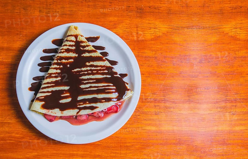 Crepe with chocolate cream and strawberry on wooden table. Sweet strawberry crepe with chocolate cream on wooden table