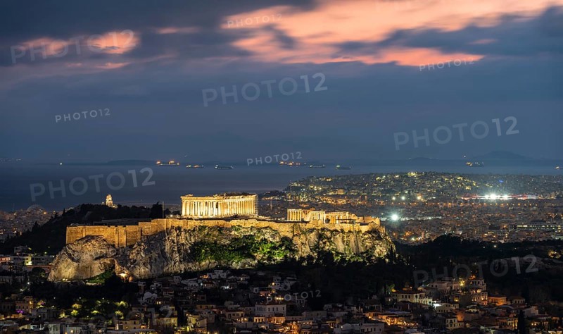 View over the sea of houses of Athens, illuminated Parthenon temple on the Acropolis, dramatic cloudy sky at sunset, from Mount Lycabettus, Athens, Greece, Europe