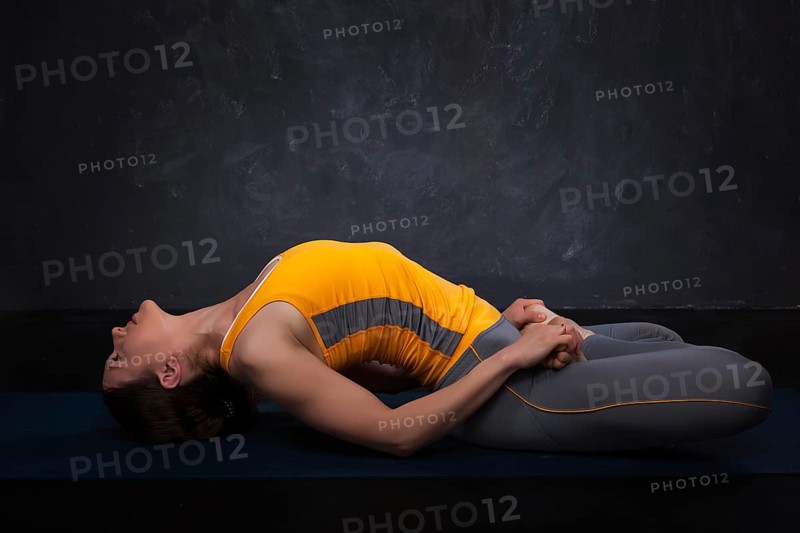 Beautiful sporty fit yogini woman practices yoga asana Matsyasana, fish pose on dark background