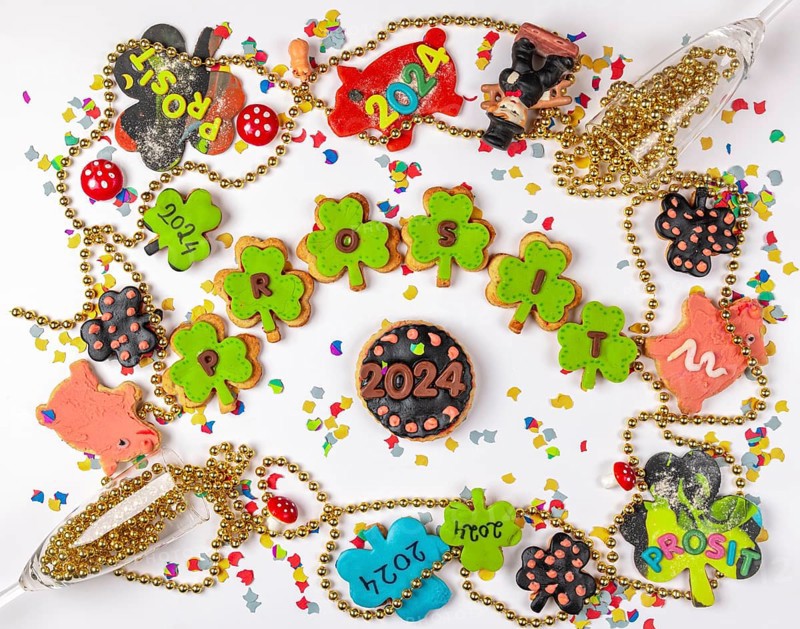 Biscuits in the shape of shamrocks, Prosit lettering, framed by lucky charms, New Year 2024, white background