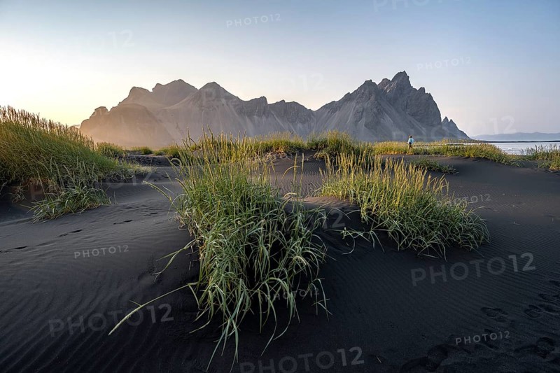 Tourist on a sand dune, Black beach with volcanic sand, Sand beach, Dunes with grass, Stokksnes headland, Klifatindur mountain range, Austurland, East Iceland, Iceland, Europe