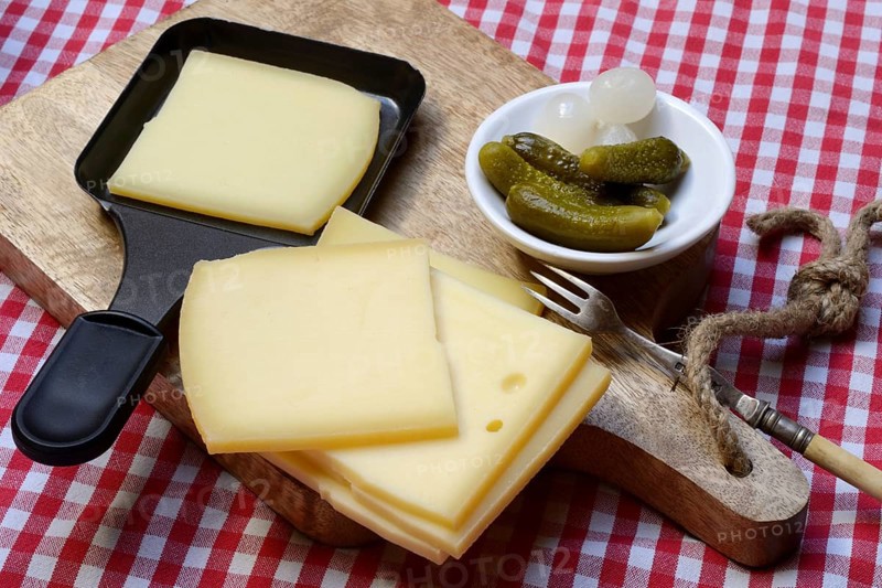 Raclette, cheese slices on wooden board and in raclette pans, Switzerland, Europe