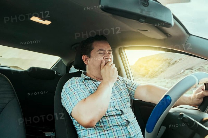 View of a sleepy driver in his car. Tired driver yawning in the car, concept of man yawning while driving. A sleepy driver at the wheel, a tired person while driving