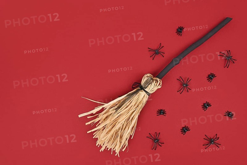 Halloween witch broom and spiders on dark red background with copy space
