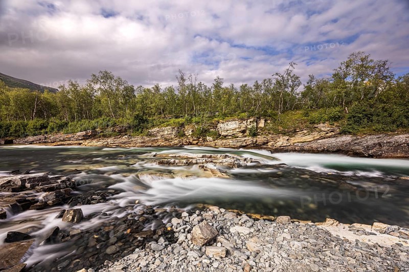 Abiskojåkka, river in Abisko NP (northern Sweden) . Long exposure, clouds, rocks, gravel, birches, forest