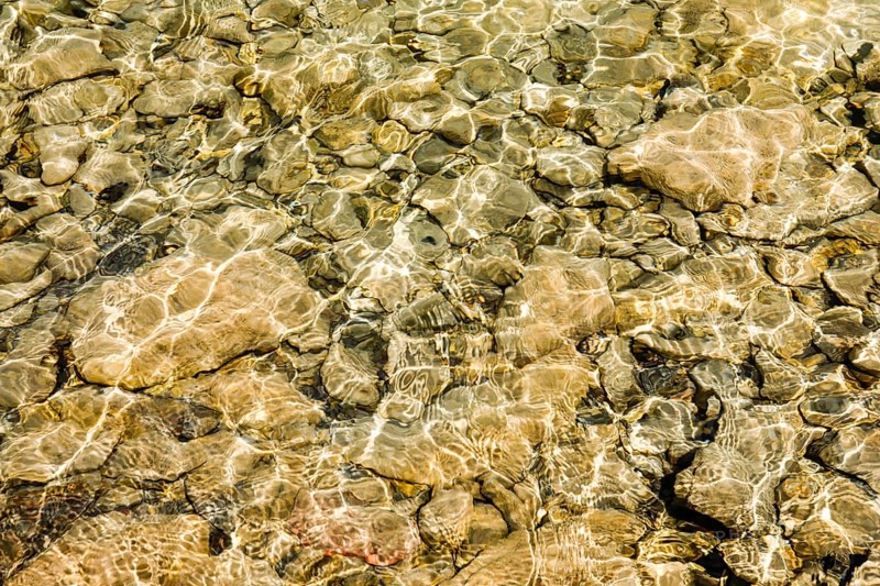 Sun casts fascinating play of light and shadow on the clear water and beige-brown stones on the shore of Lake Walen, Canton St. Gallen, Switzerland, Europe