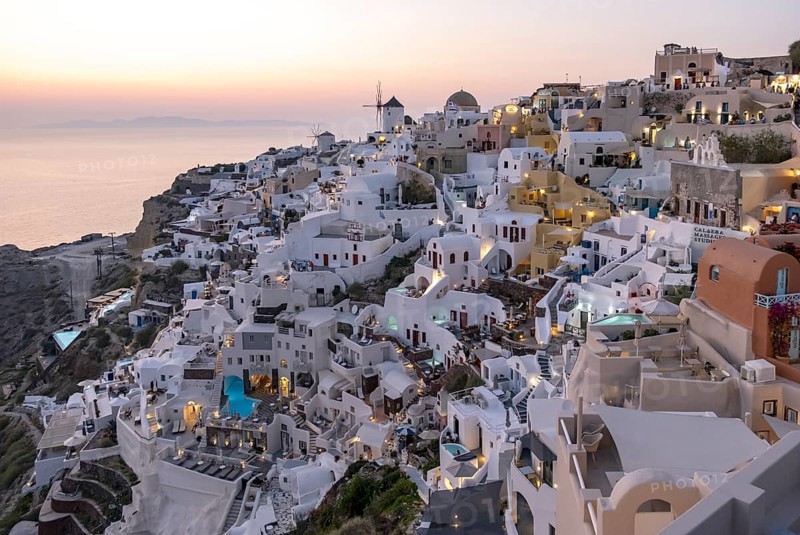 Cliff-side houses, villas and windmill in the village of Ia seen from Oia Castle at dusk, Santorini, Greece, Europe