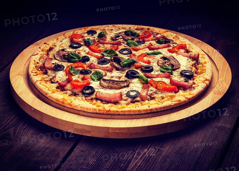 Vintage retro effect filtered hipster style image of ham pizza with (capsicum), mushrooms, olives and basil leaves on wooden board on old table