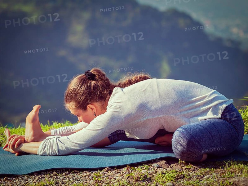 Yoga outdoors, woman doing Ashtanga Vinyasa yoga Janu Sirsasana A head to knee stretching asana position outdoors. Vintage retro effect filtered hipster style image