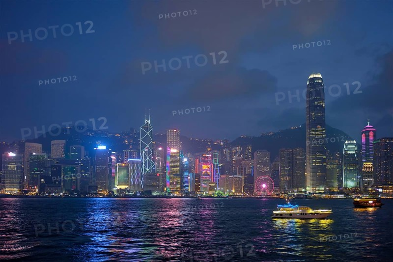 Hong Kong skyline cityscape downtown skyscrapers over Victoria Harbour in the evening illuminated with tourist boat ferries. Hong Kong, China, Asia