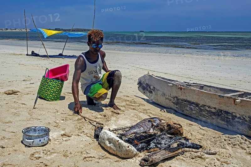 Malagasy man cooking freshly caught fish on grill over charcoal fire on sandy beach at Andavadoaka near Morombe, Atsimo-Andrefana Region, Madagascar, Africa