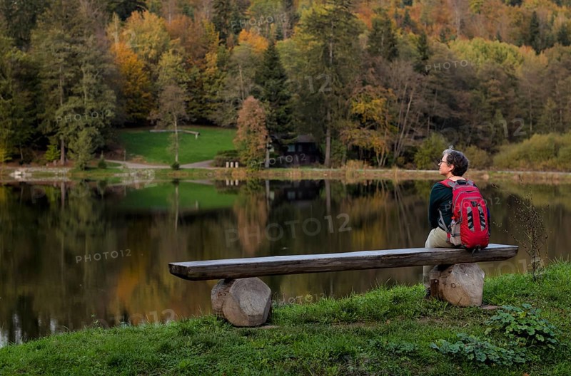 Older woman with backpack, Best Ager, sitting lonely on wooden bench, Ebnisee, Kaisersbach, autumn, Swabian Forest, Baden-Württemberg, Germany, Europe