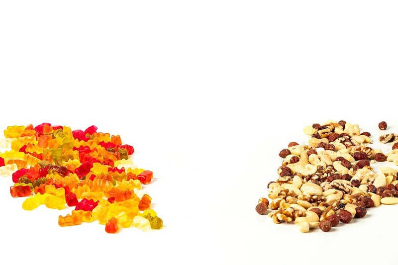 Comparison of unhealthy and healthy, gummy bears and various nuts, on white, copy room
