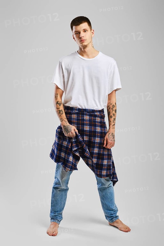 Young cocky man in t-shirt, jeans and checkered shirt tied at the waist