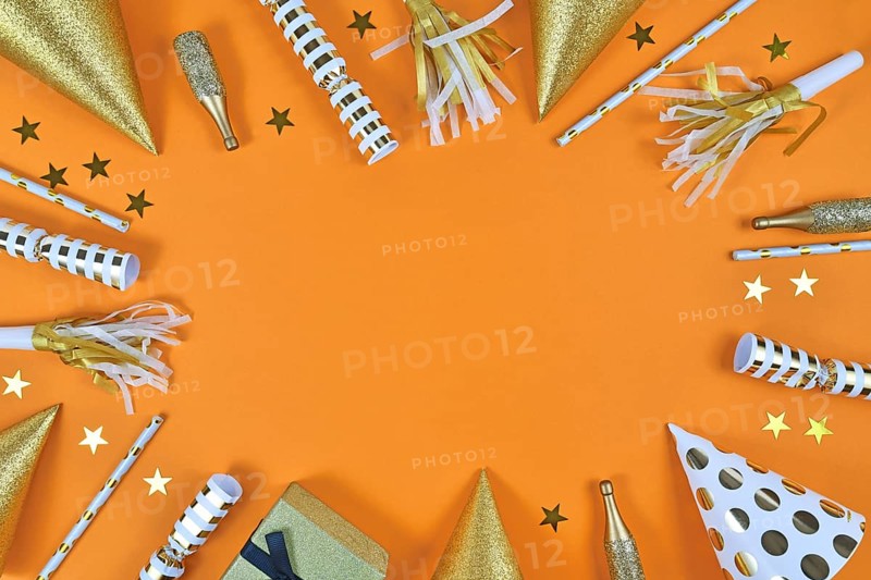 Party objects like paper hats, confetti, golden champagne bottles and star confetti forming frame around orange background