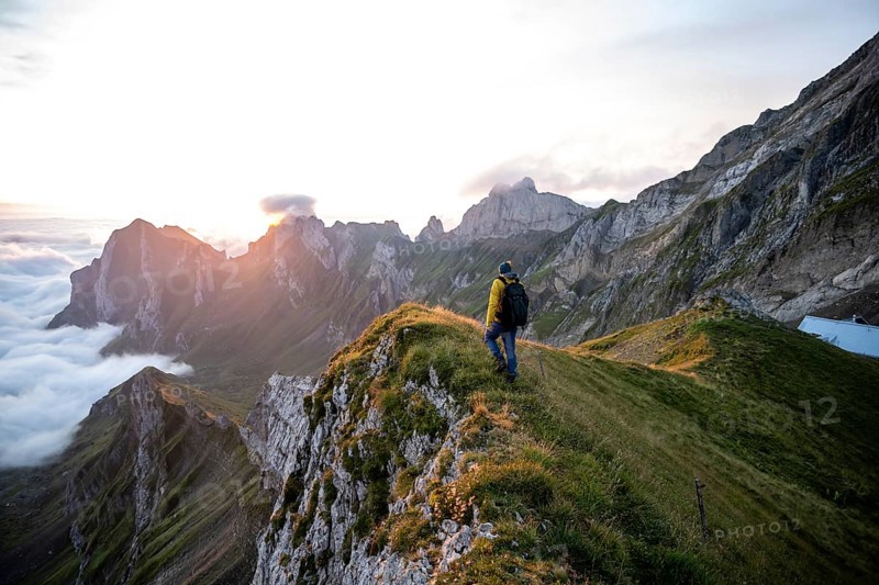Hiker enjoying the view over the Säntis mountains into the valley of Meglisalp at sunrise, high fog in the valley, Säntis, Appenzell Ausserrhoden, Appenzell Alps, Switzerland, Europe