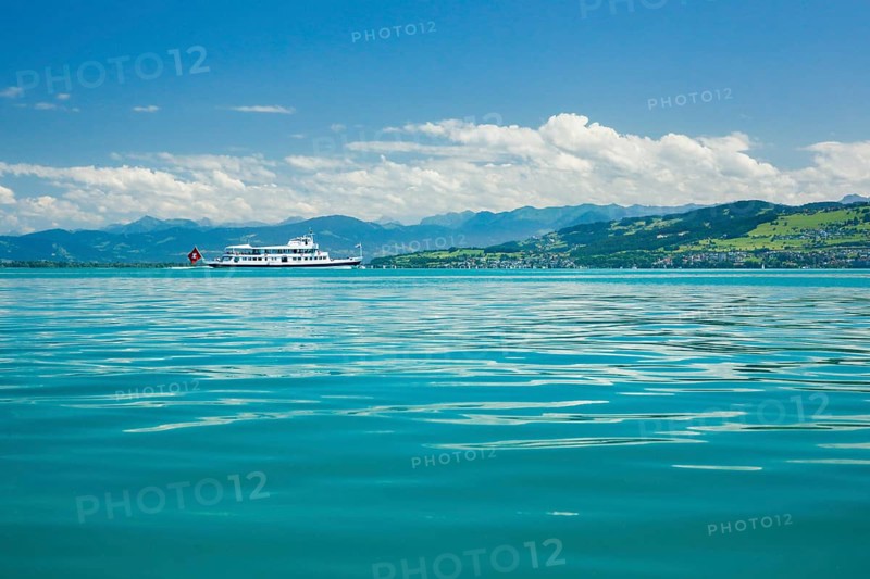 Course ship with Swiss flag on the turquoise waters of Lake Constance in front of the Austrian Alps