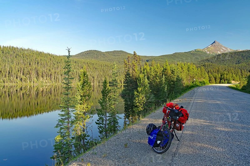 Bicycle standing by a crystal clear lake on an empty road, evening light, Stewart Cassiar Highway, British Columbia, Canada, North America