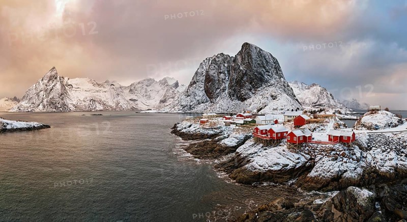 Panorama of famous tourist attraction Hamnoy fishing village on Lofoten Islands, Norway with red rorbu houses. With falling snow in winter on sunrise