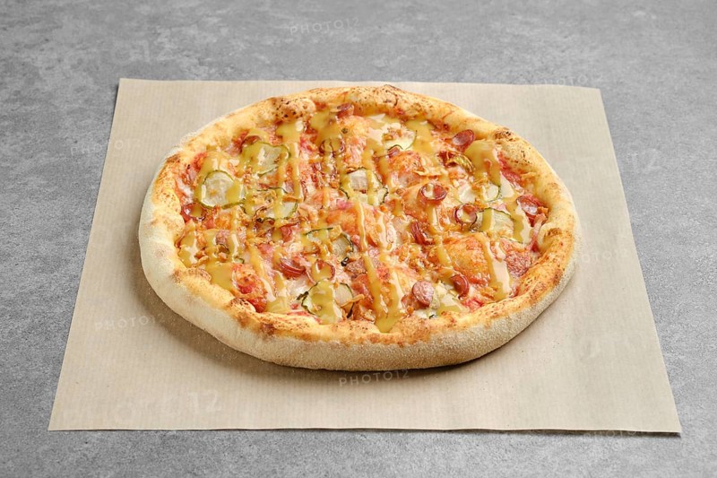 Top view of pizza with thin sausage and pickled cucumber on parchment paper
