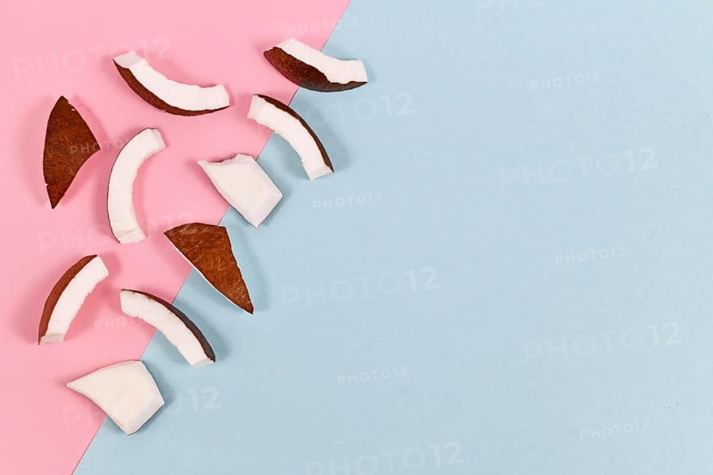 Pieces of coconut fruit on left side of light blue and pink background with blank copy space