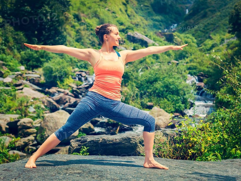 Yoga outdoors, sporty fit woman doing Ashtanga Vinyasa Yoga asana Virabhadrasana 2 Warrior pose posture at tropical waterfall. Vintage retro effect filtered hipster style image