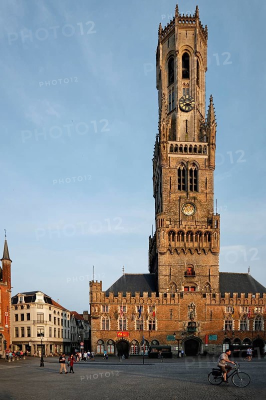 BRUGES, BELGIUM, MAY 28, 2018: Belfry tower famous tourist destination and Grote markt square in Bruges, Belgium with pedestrians and bicycle on sunset